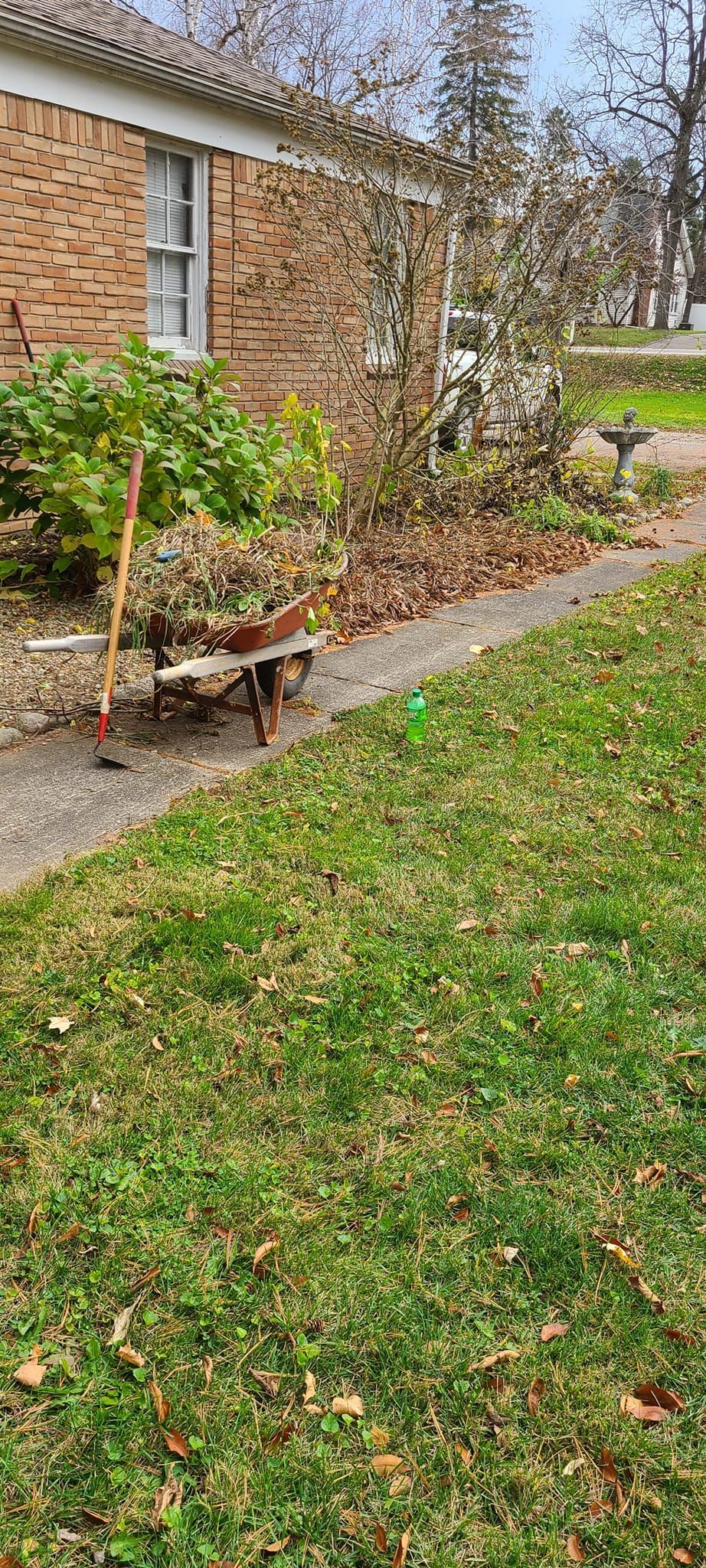 A wheelbarrow is sitting in the grass in front of a brick house.