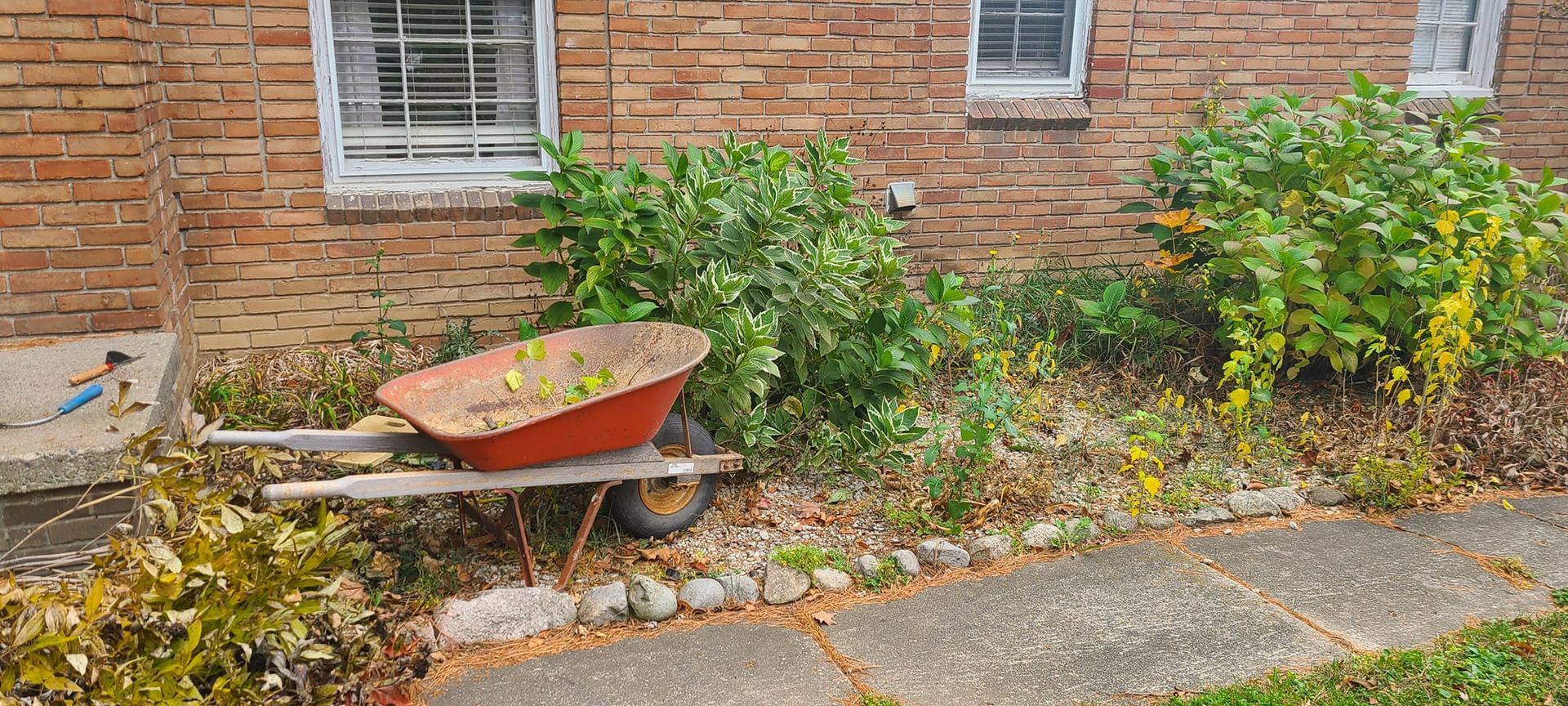 A red wheelbarrow is parked in front of a brick building.