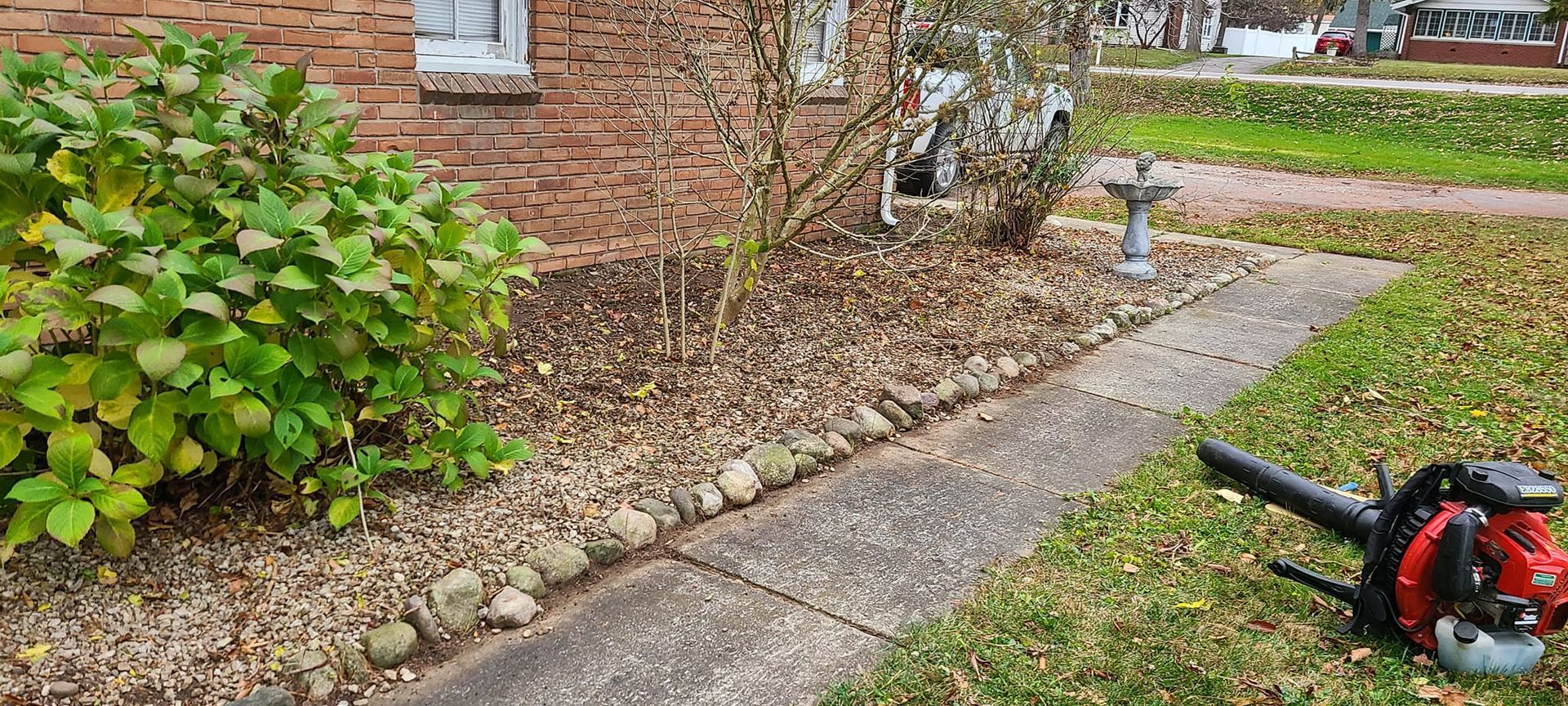 A leaf blower is sitting on the sidewalk in front of a house.