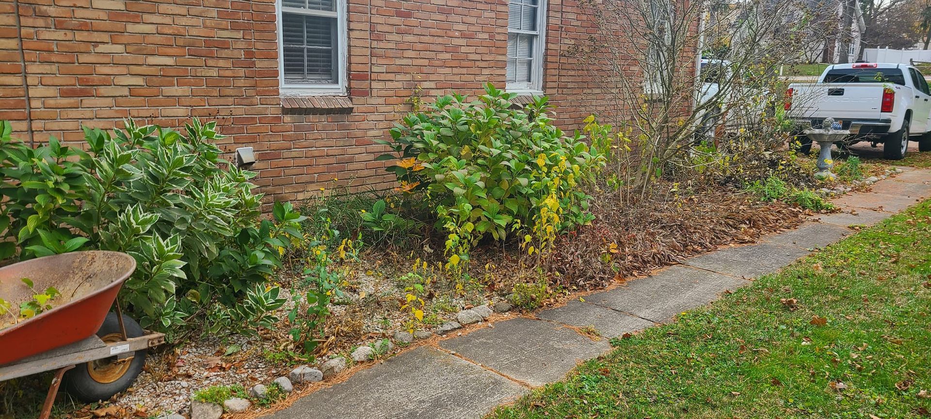 A wheelbarrow is parked on the sidewalk in front of a brick house.