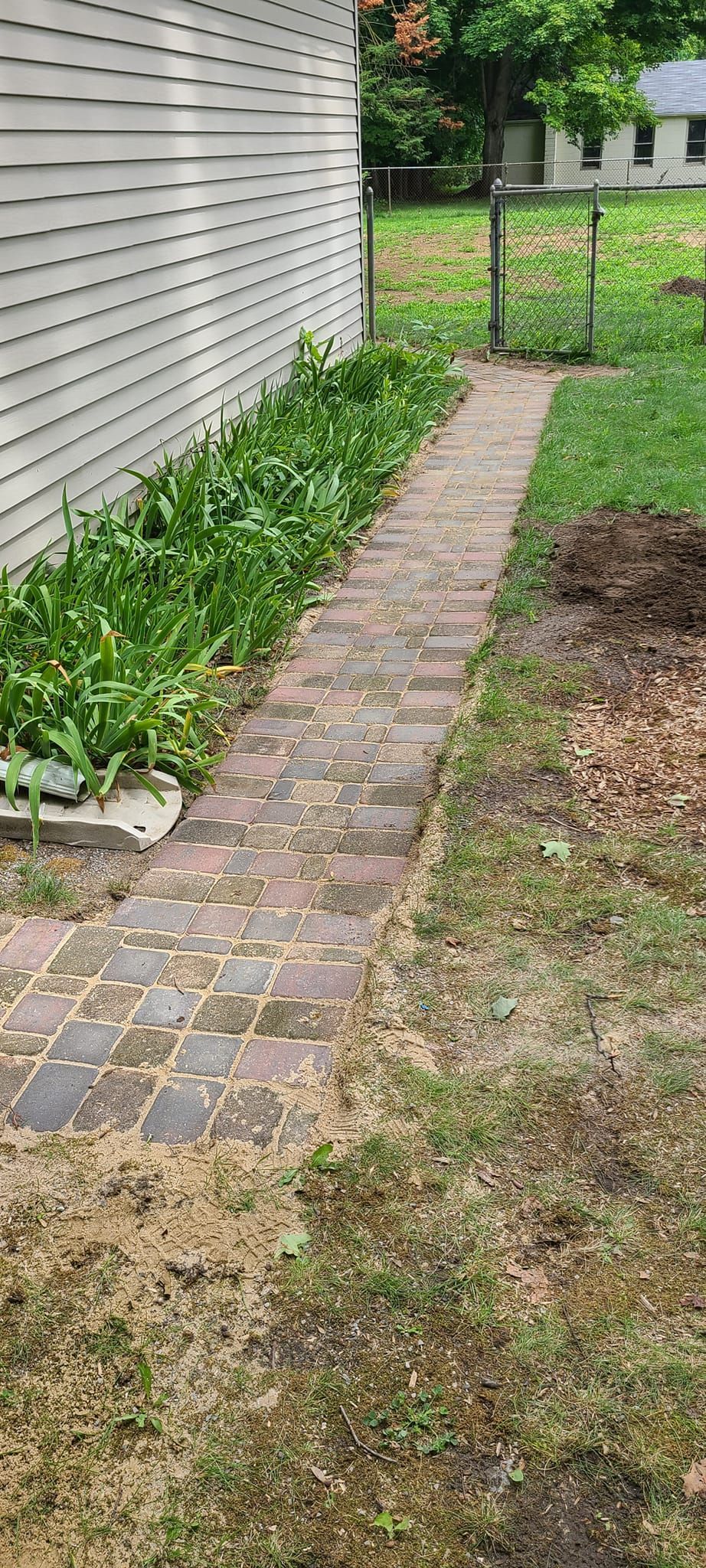 A brick walkway leading to a house in a backyard.