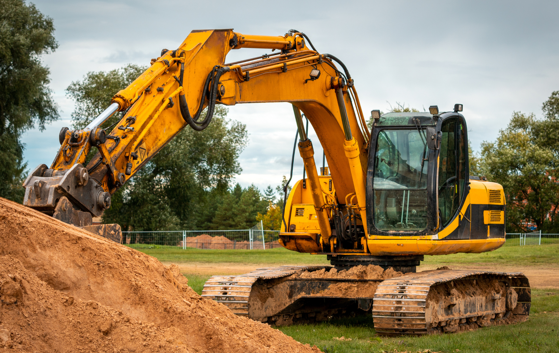 A yellow excavator is digging a pile of dirt in a field.