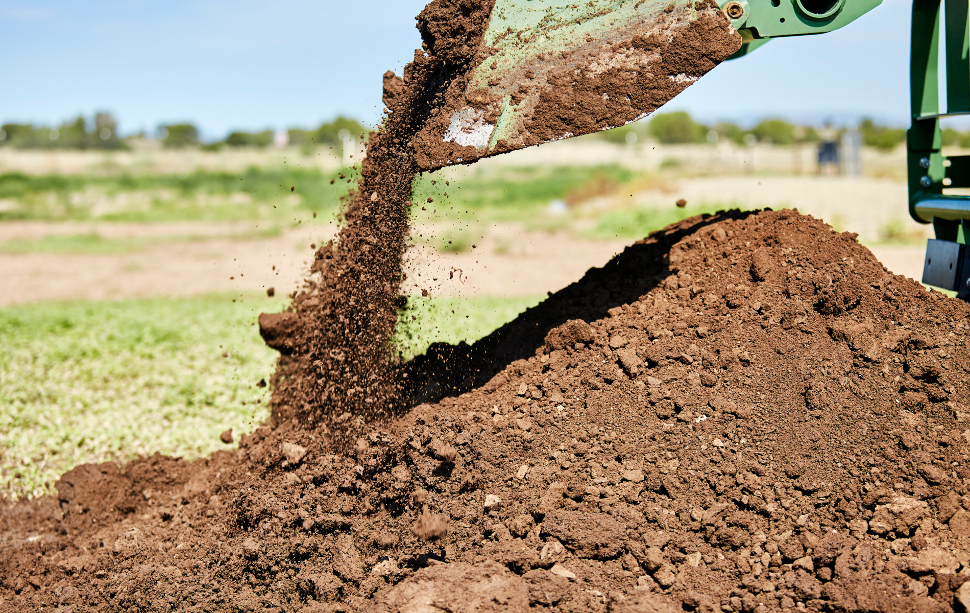 A pile of dirt is being poured from a machine into a field.