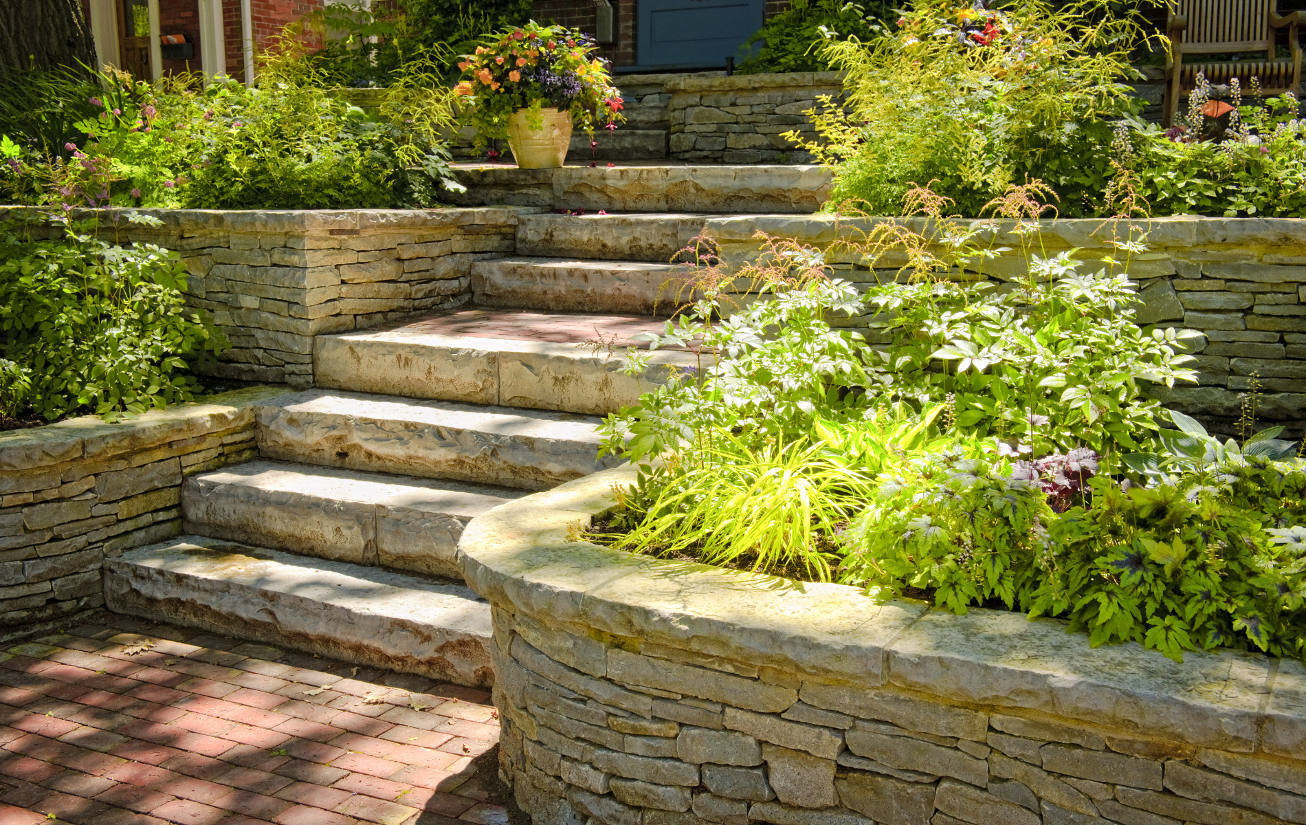 A stone wall surrounds a set of stairs leading up to a house.