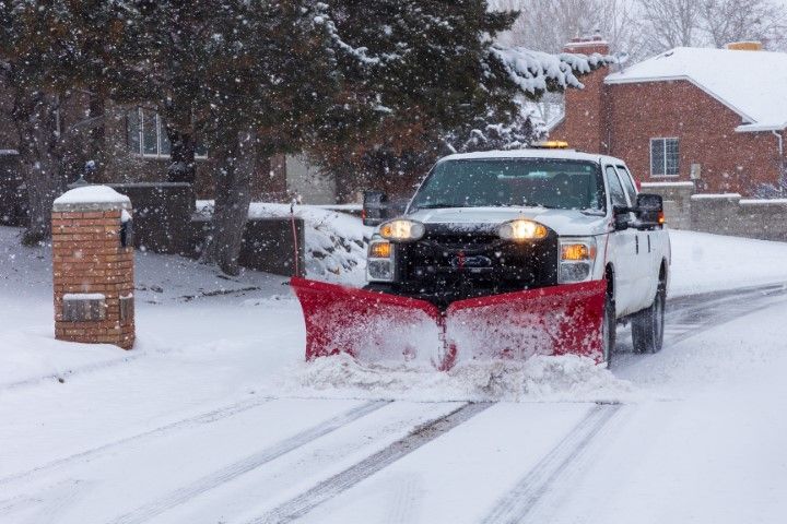 Pickup truck with red snowplow clearing a snowy residential street during snowfall