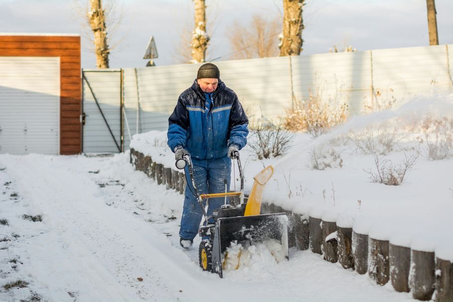 Person clearing snow with a snow blower in a snowy driveway