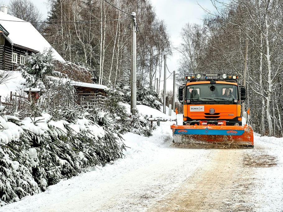 Orange snowplow clearing a snowy road in a winter neighborhood
