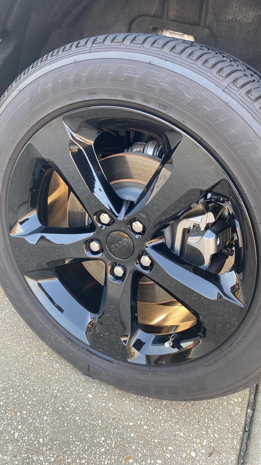A close up of a black car wheel on a sidewalk.