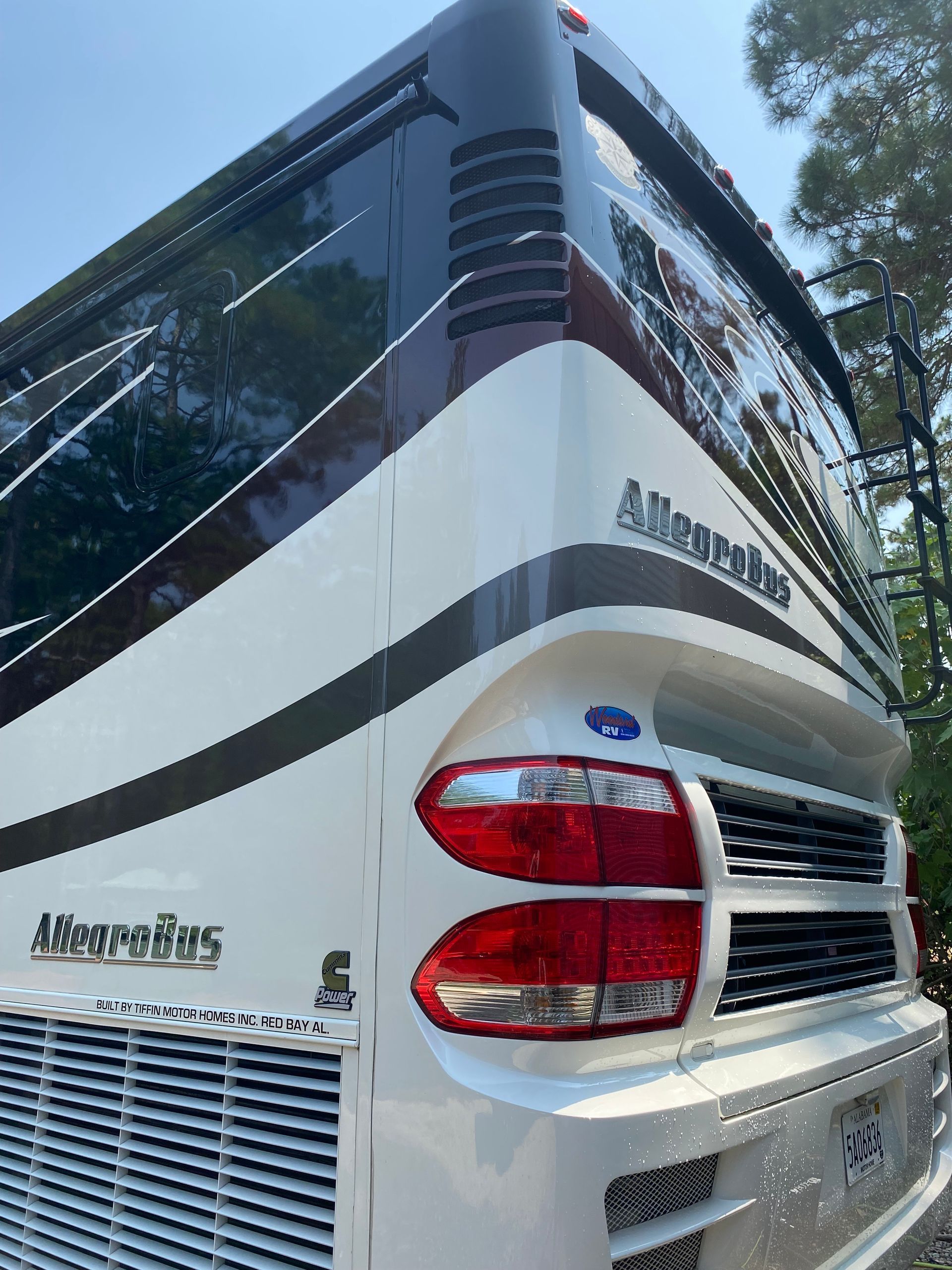 A white allegro bus is parked in the woods