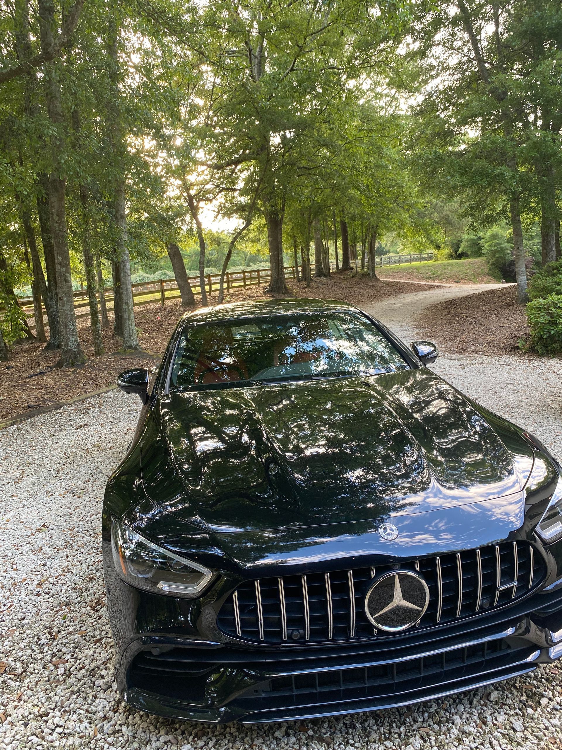 A black mercedes benz is parked in a gravel driveway surrounded by trees.