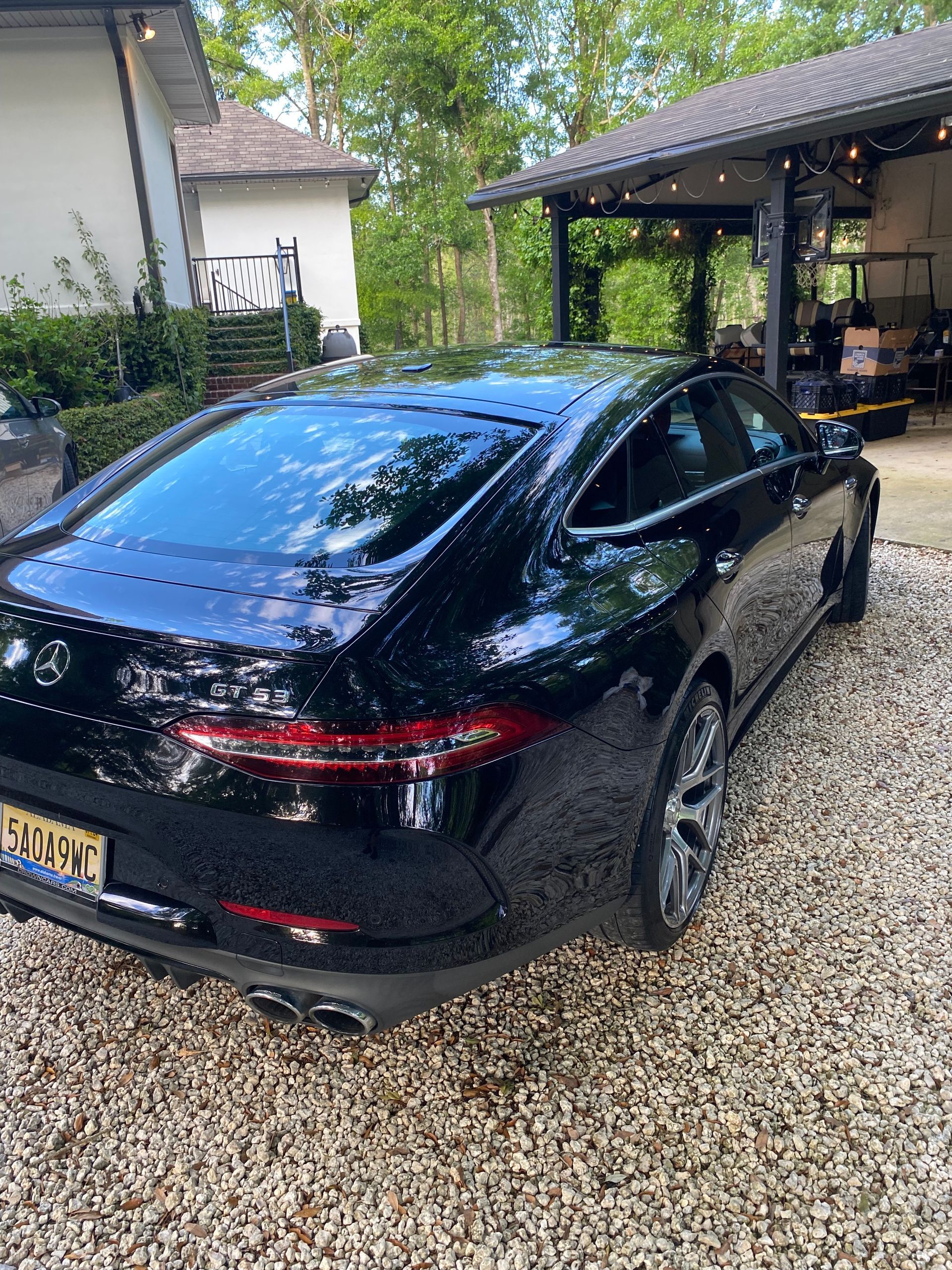 A black mercedes benz is parked in a gravel driveway in front of a house.