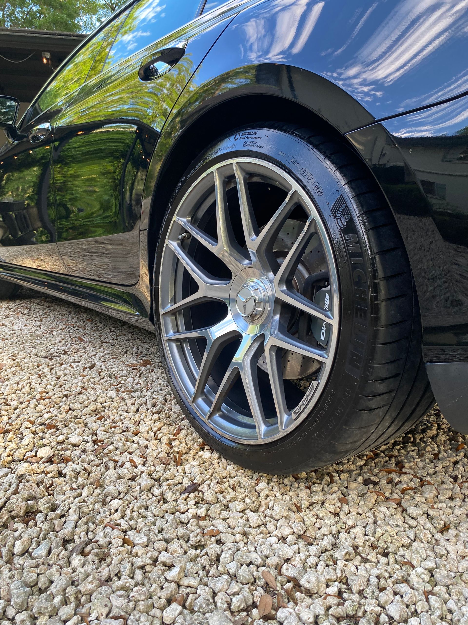A black car is parked on gravel in a driveway.