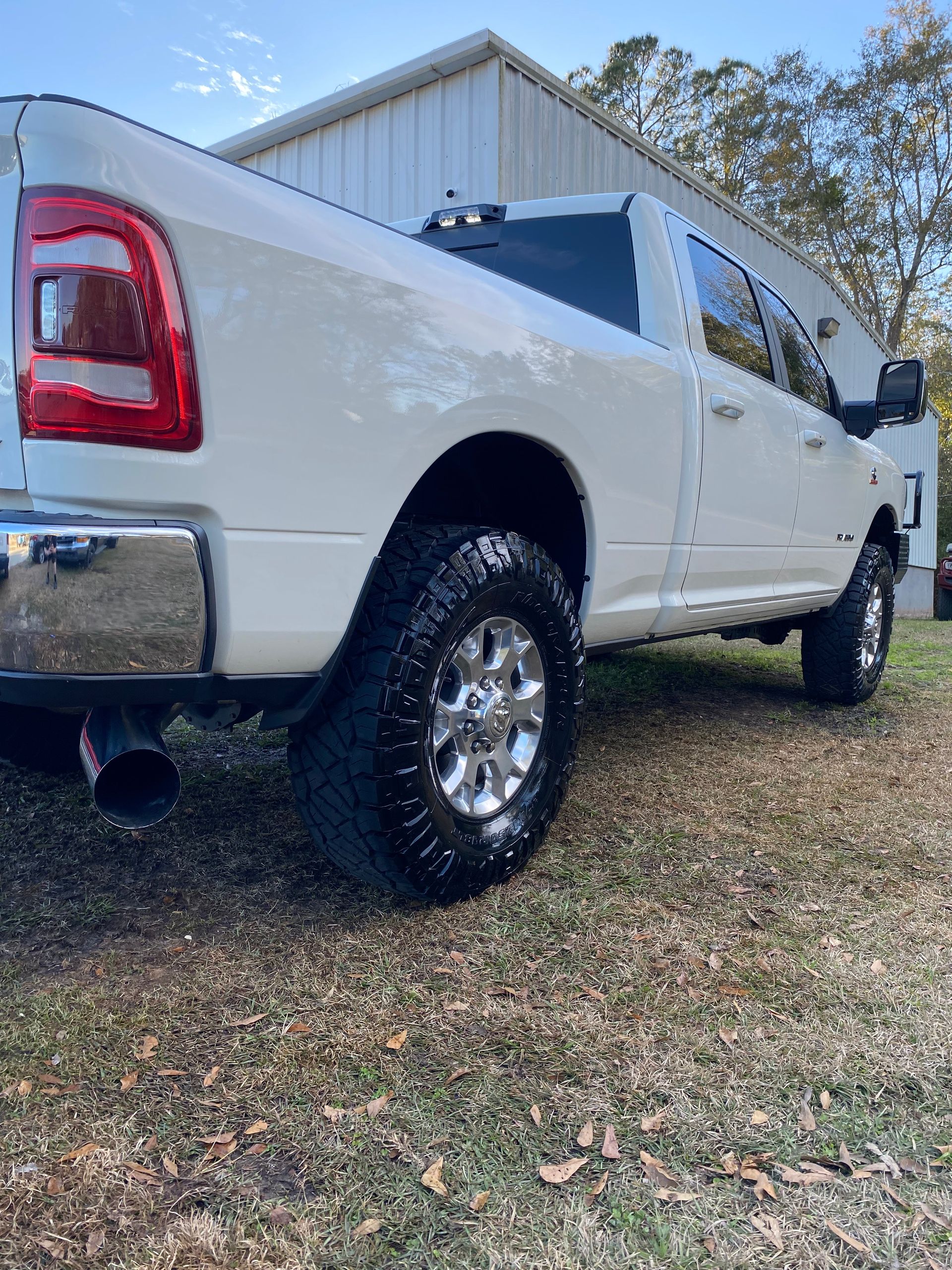 A white dodge ram truck is parked in a grassy area in front of a building.