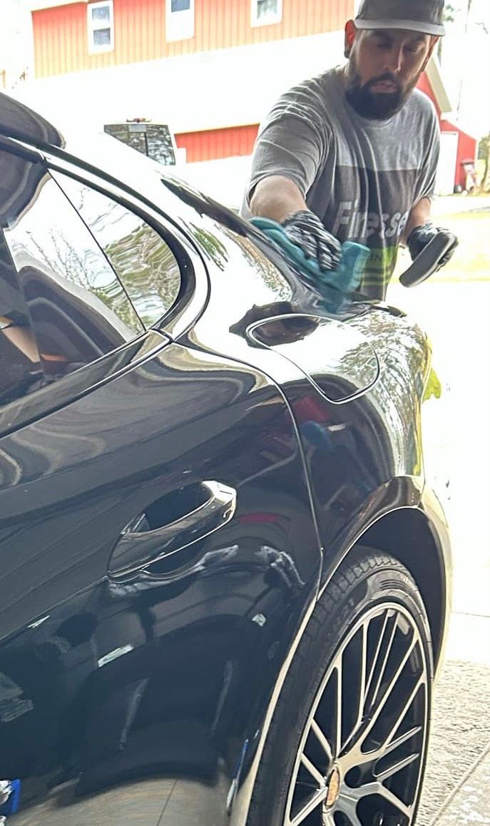 A man is cleaning the windshield of a black car.
