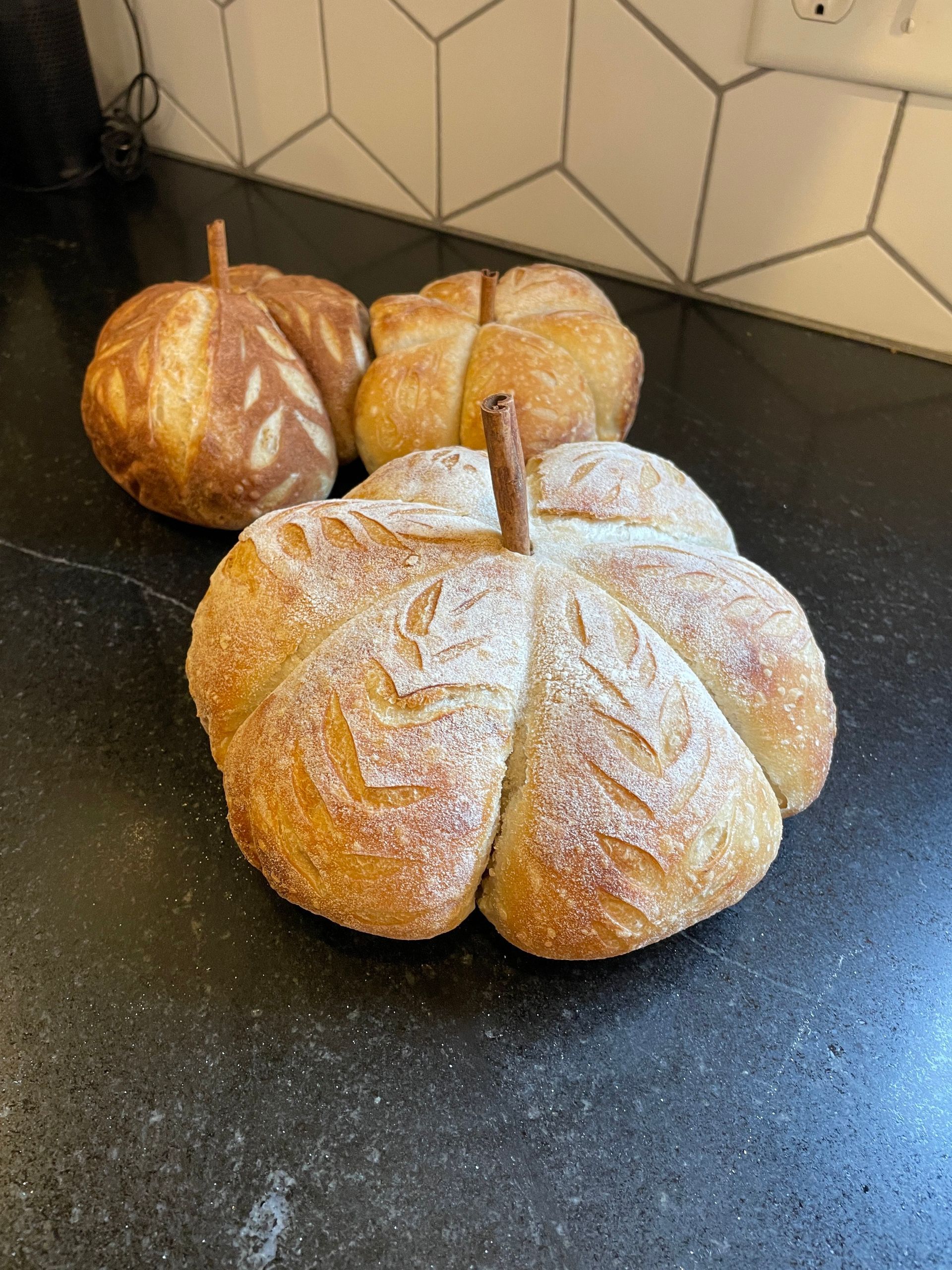 Three loaves of bread in the shape of pumpkins are sitting on a counter.