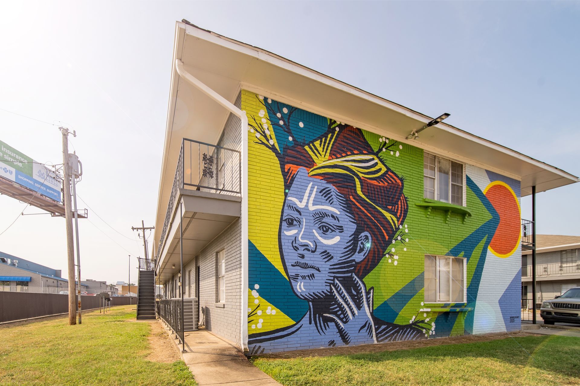 Colorful mural on a beige building wall beside a sidewalk and utility poles under a clear sky