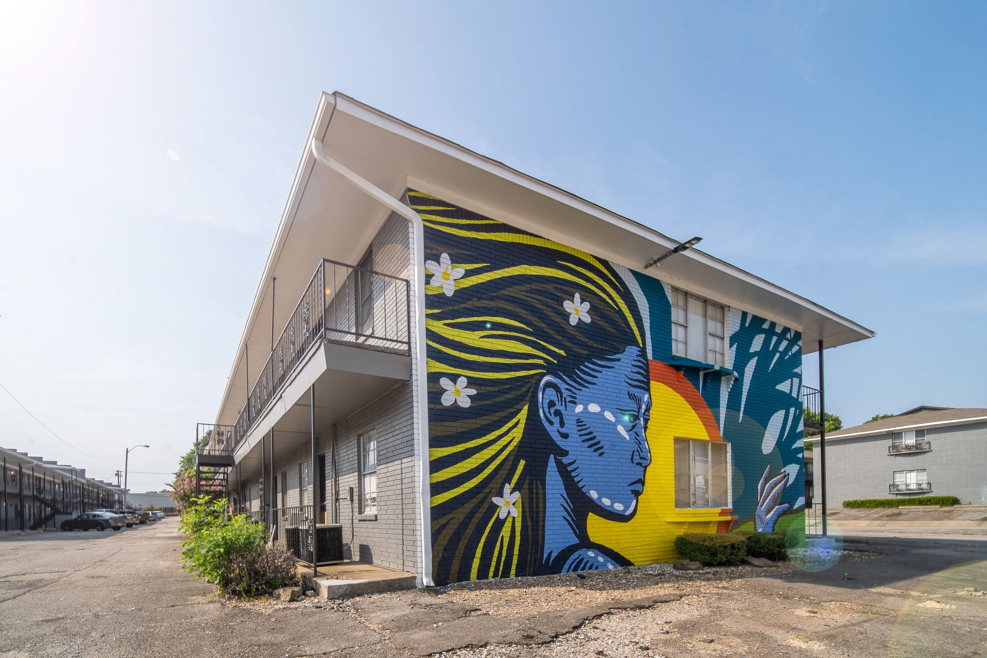 Mural of a blue face with yellow hair on a two-story building under a clear sky