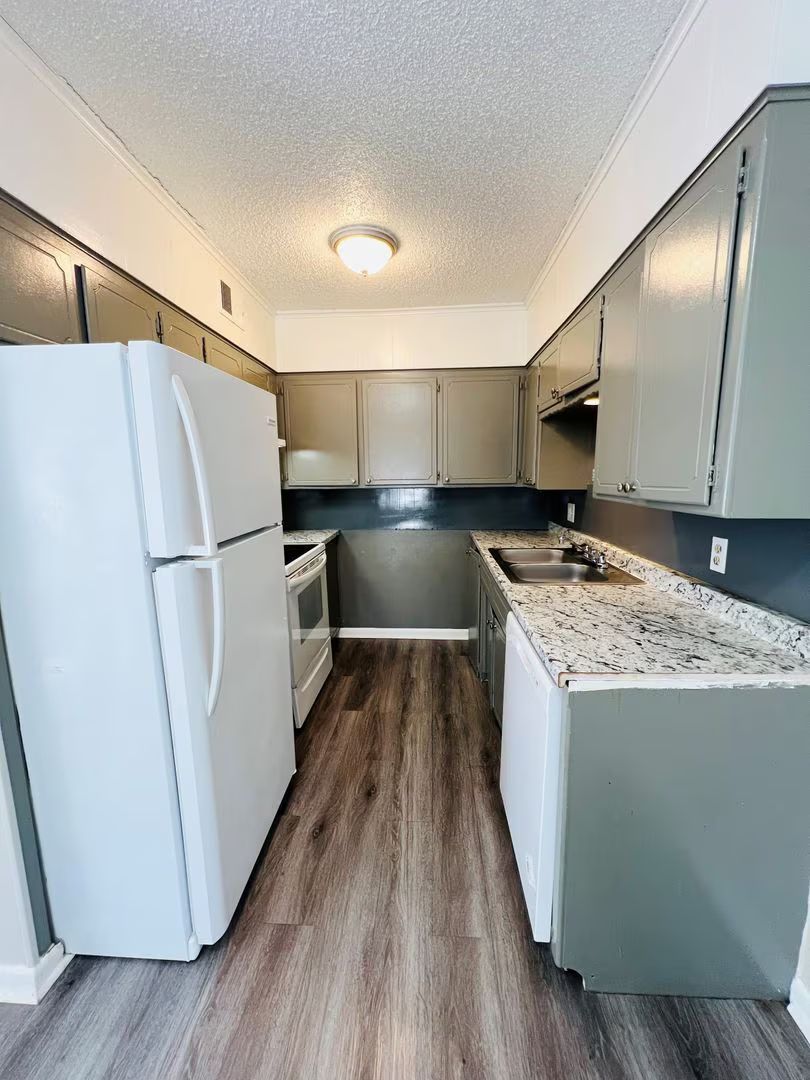 Small galley kitchen with white cabinets, refrigerator, granite counters, and wood-look floor.