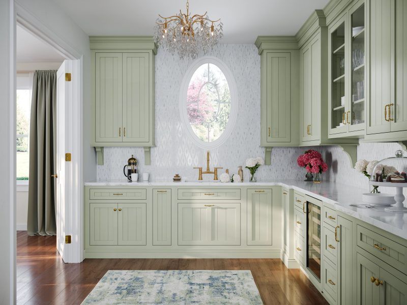 A kitchen with green cabinets , white counter tops , a rug and a window.