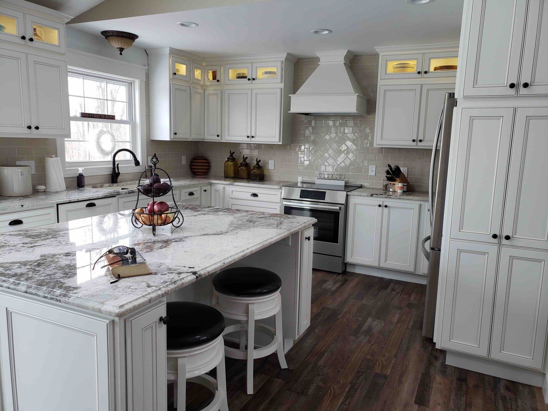 A kitchen with white cabinets , granite counter tops , stools and a large island.