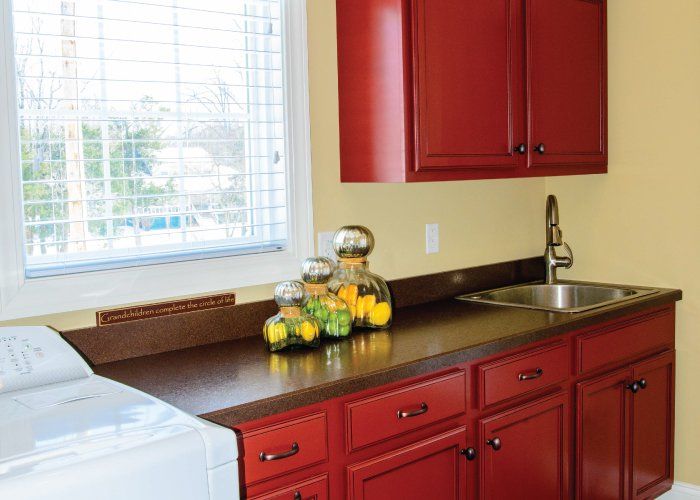 A laundry room with red cabinets , a washer and dryer , a sink , and a window.