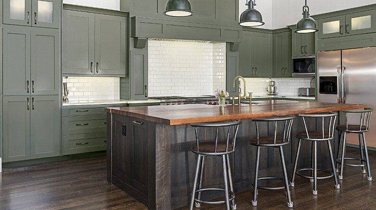 A kitchen with green cabinets , stainless steel appliances , a large island and stools.