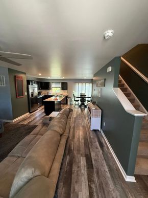 Long living room with sectional sofa, wood floors, staircase, and kitchen in the background