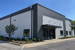Empty strip mall storefront with glass windows, tan facade, and black awnings on a sunny street corner