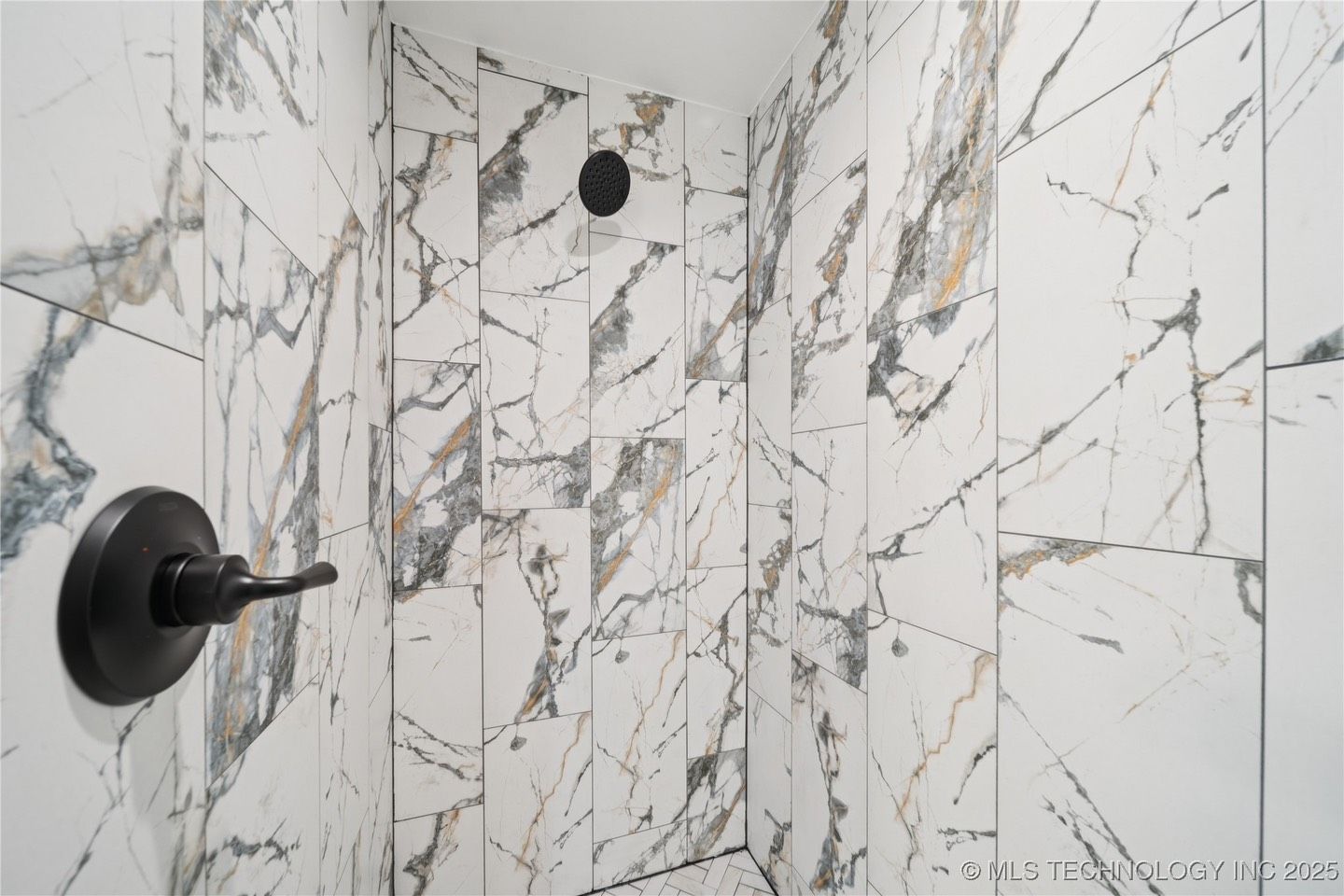 A bathroom with marble tiles and a black shower head.