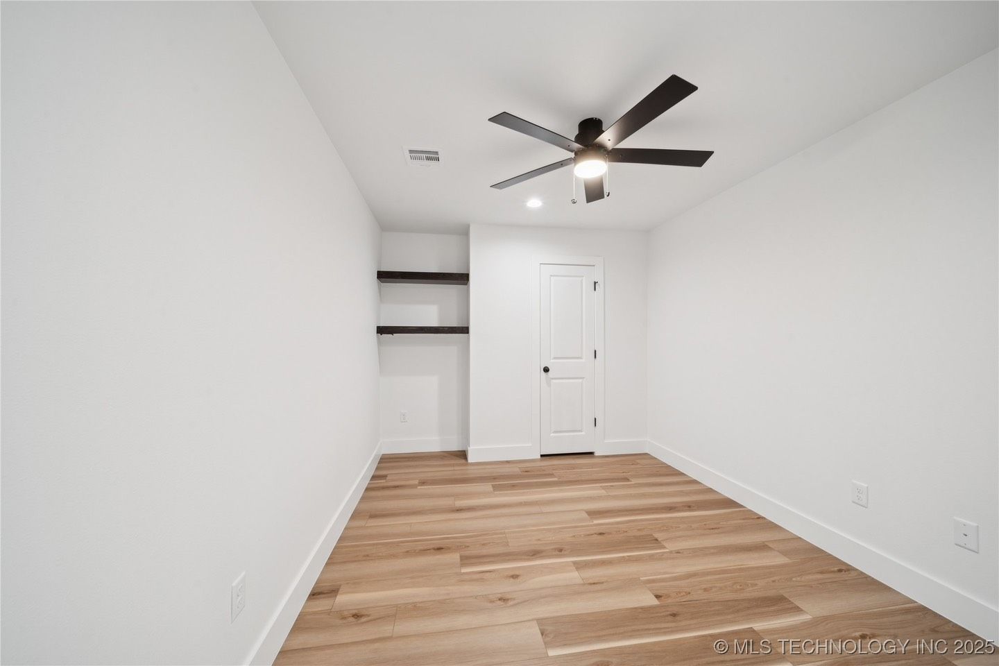 An empty room with hardwood floors and a ceiling fan.