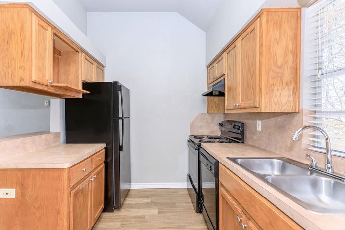 Kitchen with wood cabinets, black appliances, and a double sink near a window.