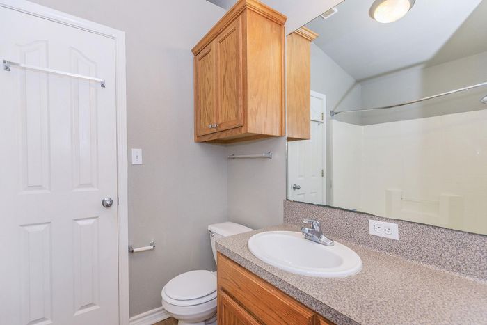 Bathroom with a sink, toilet, wooden cabinets, and a mirror. White door on the left.