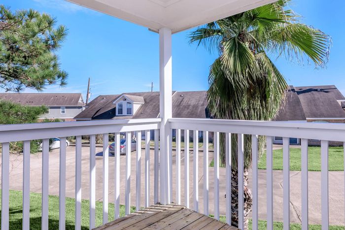 Balcony view: white railing, palm tree, houses, blue sky.