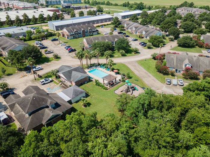 Aerial view of an apartment complex with a pool, playground, and parking, surrounded by trees.