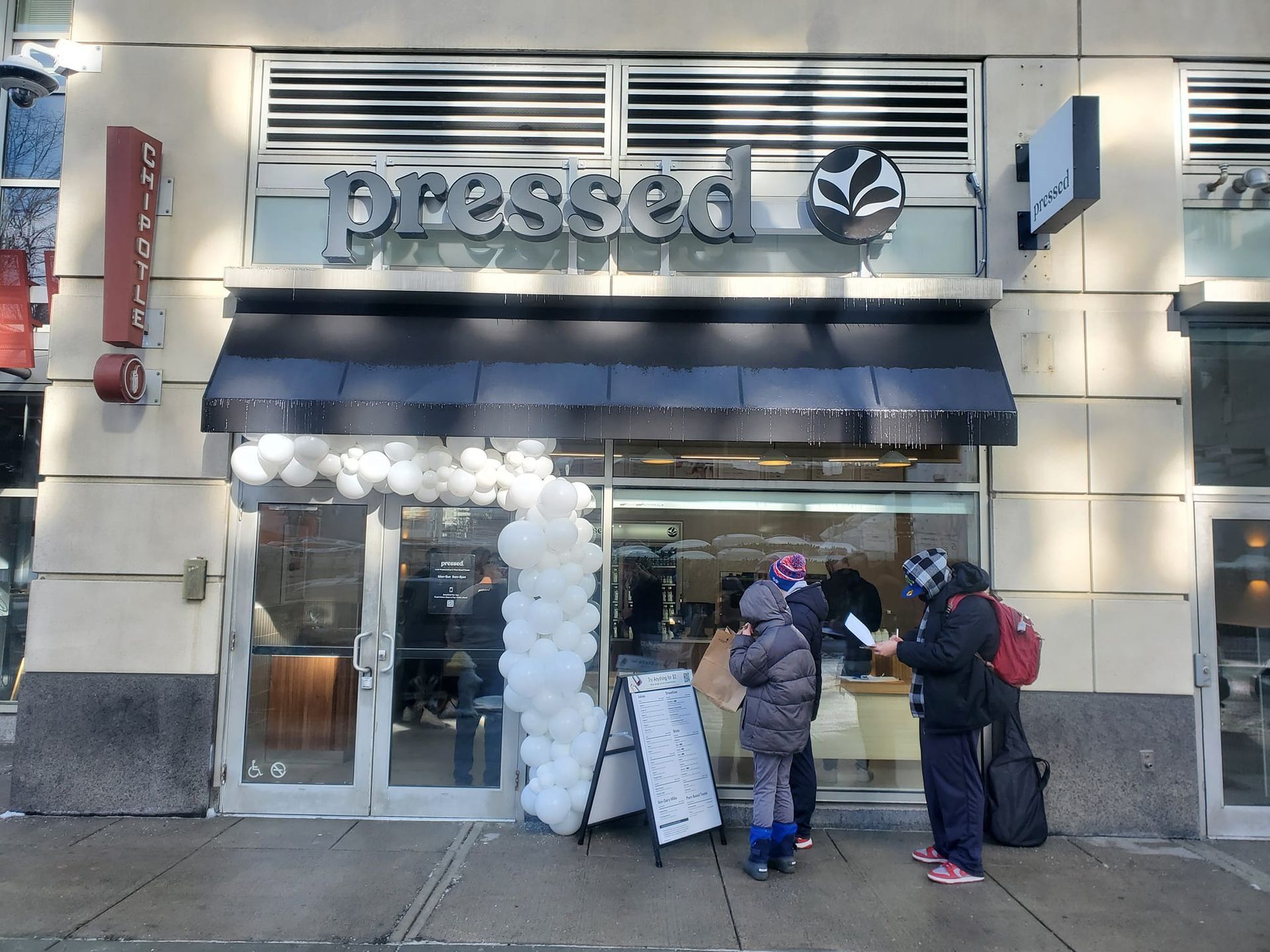 A group of people standing outside of a pressed coffee shop