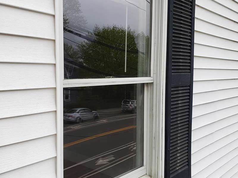 A window on the side of a white house with black shutters