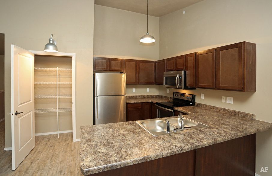 Kitchen with granite island, dark wood cabinets, stainless appliances, and a pantry door open.