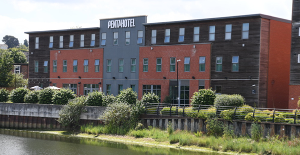 Brick house with white windows, arched doorway, and brown roof on a sunny street.
