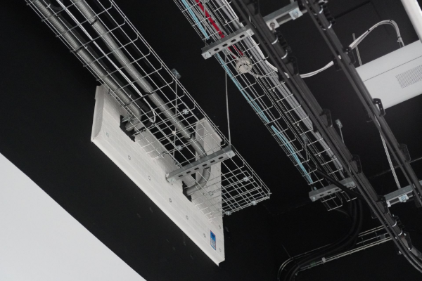 Overhead view of electrical wiring and ventilation systems installed on a black ceiling.