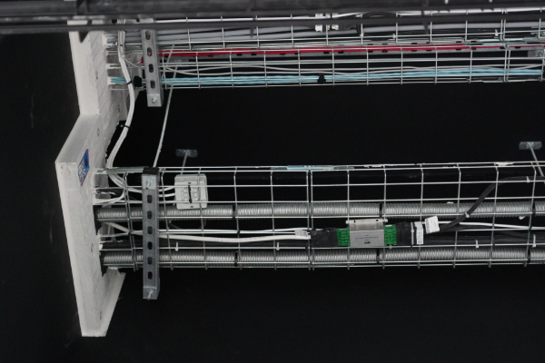 Metal wire cable trays with electrical wiring against a black background.