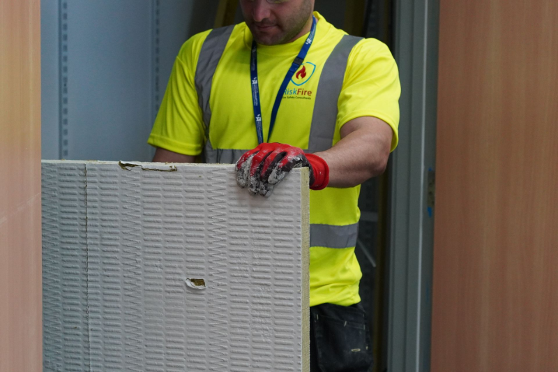 Construction worker in yellow vest and gloves, holding a textured panel.