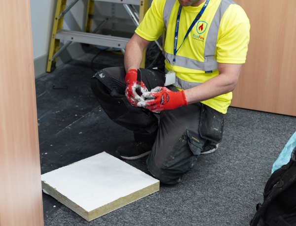 Person in safety vest and gloves preparing insulation panel indoors.