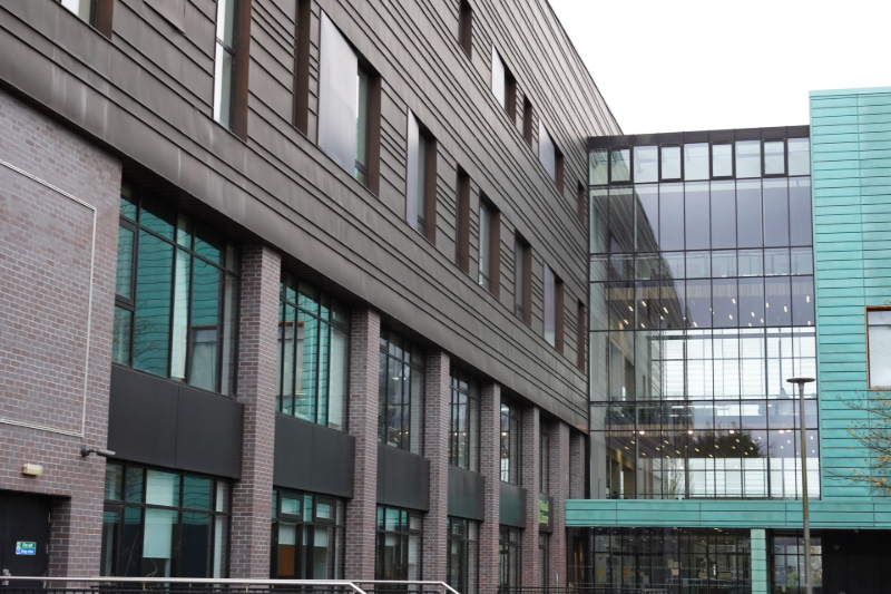 Modern building exterior with dark gray and turquoise panels, large windows, and a brick base.