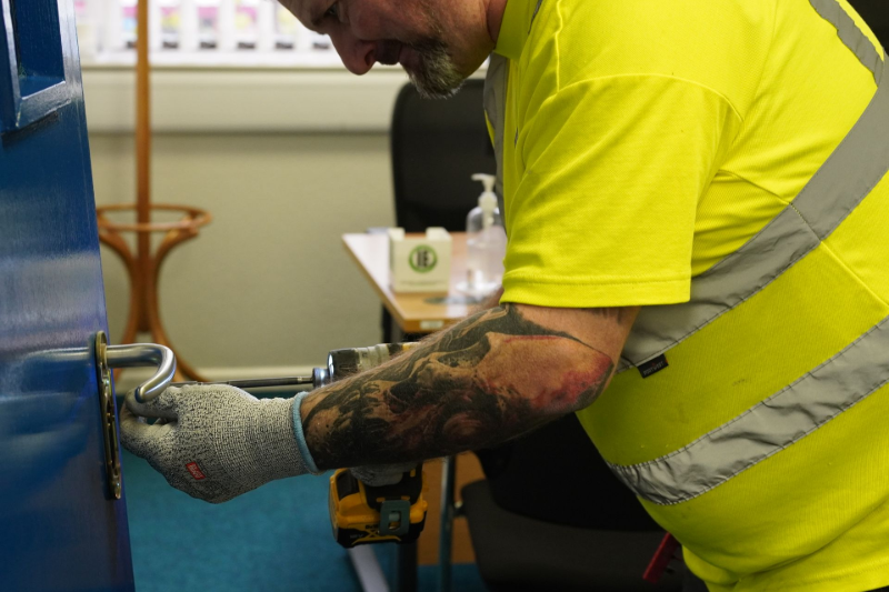 Person wearing yellow shirt and gloves installing a door handle.