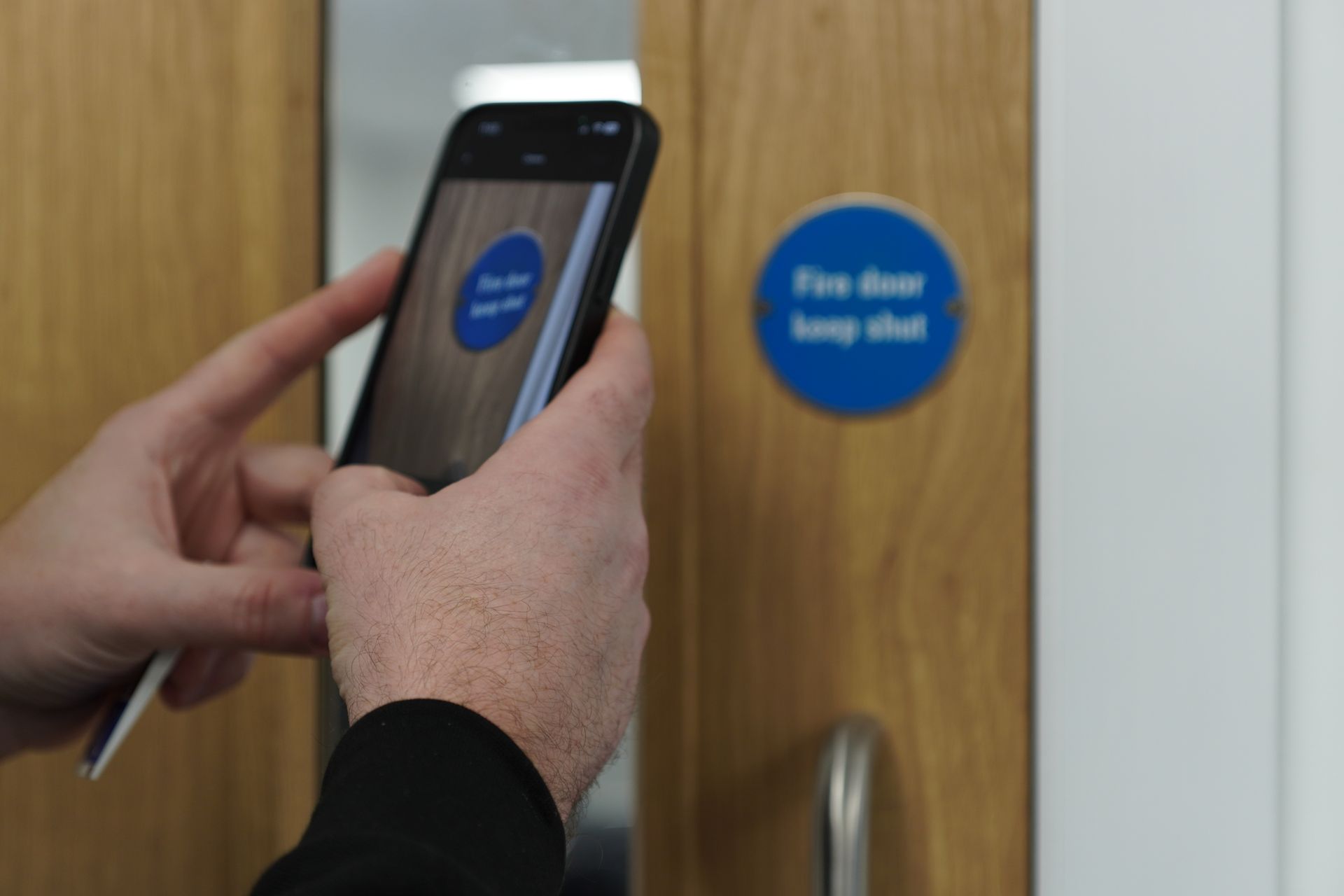 Two people in high-visibility vests install a white door in a hallway.