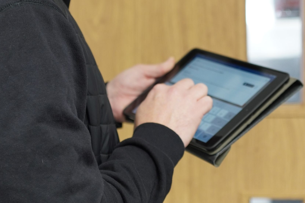 Man in black vest using a tablet, standing in front of a wooden door.