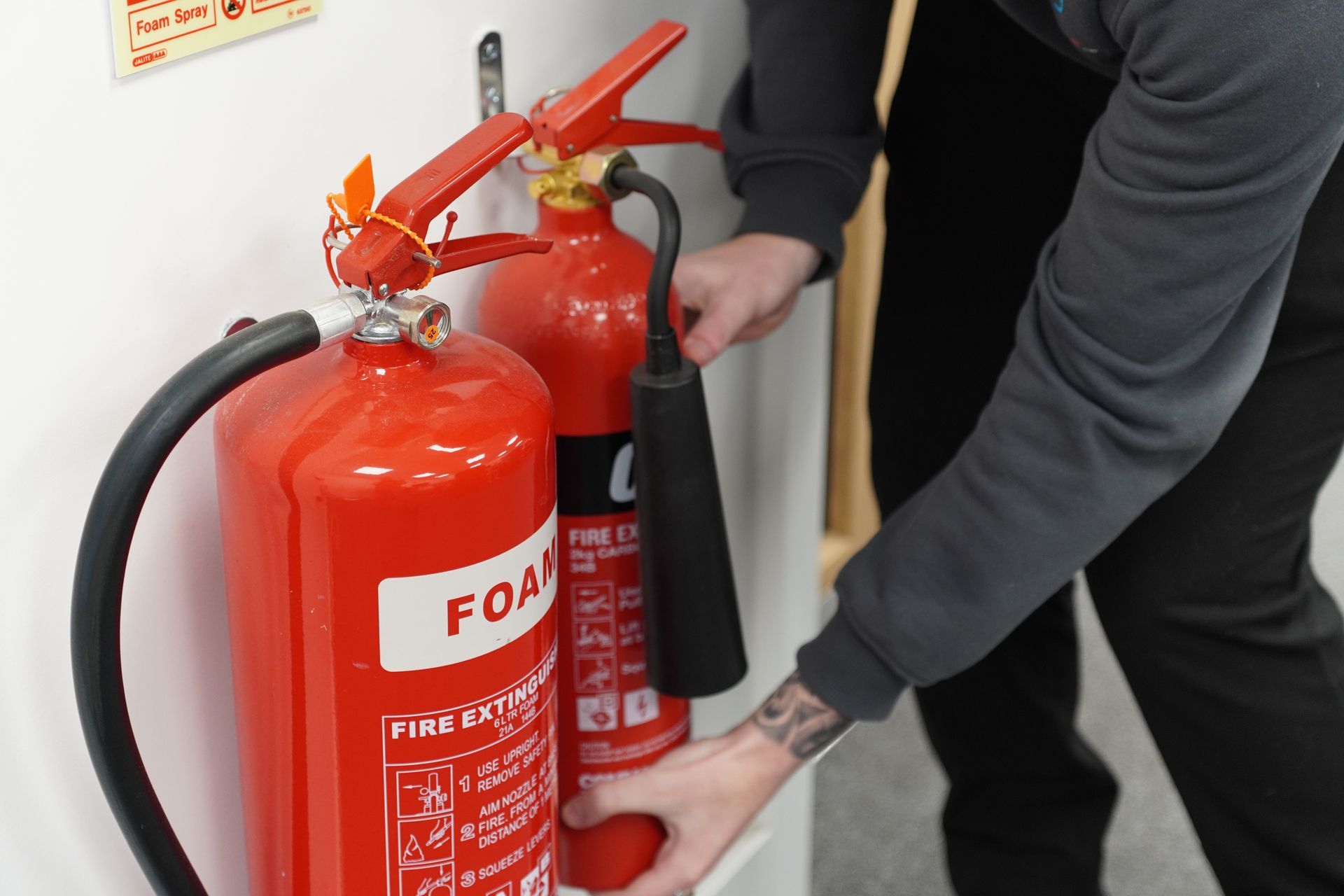 A red fire extinguisher is sitting in a corner of a room next to a red wall.