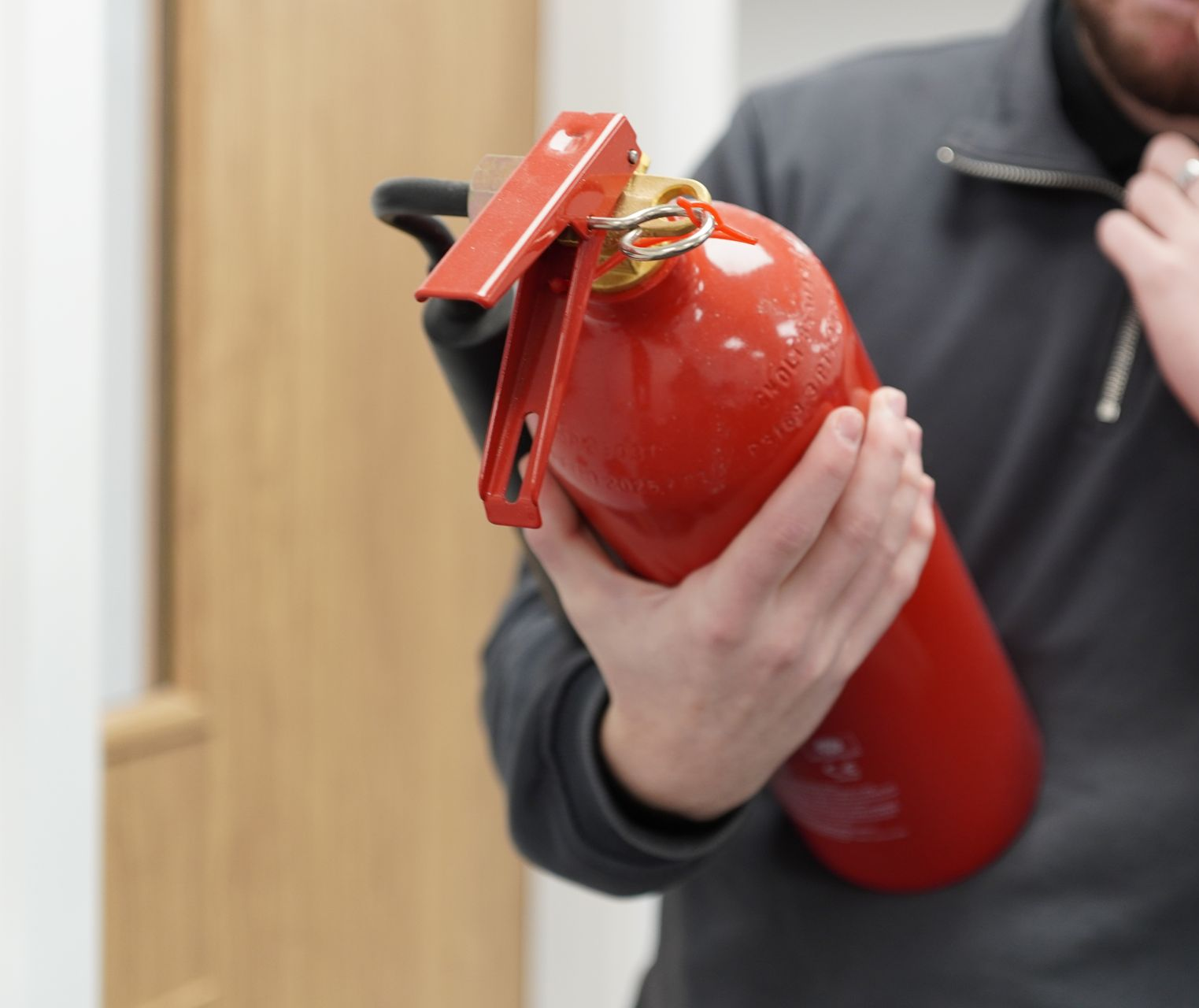 A red fire extinguisher is hanging on a white wall