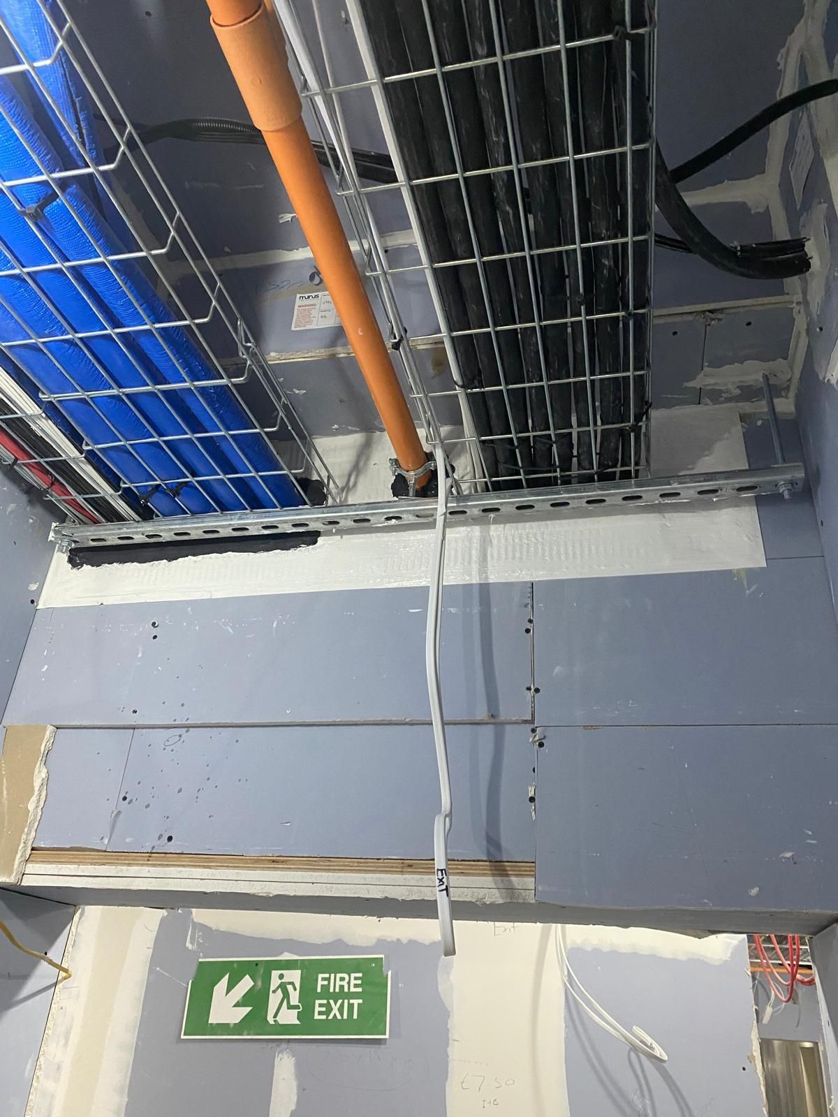 A fire exit sign is hanging from the ceiling of a building.