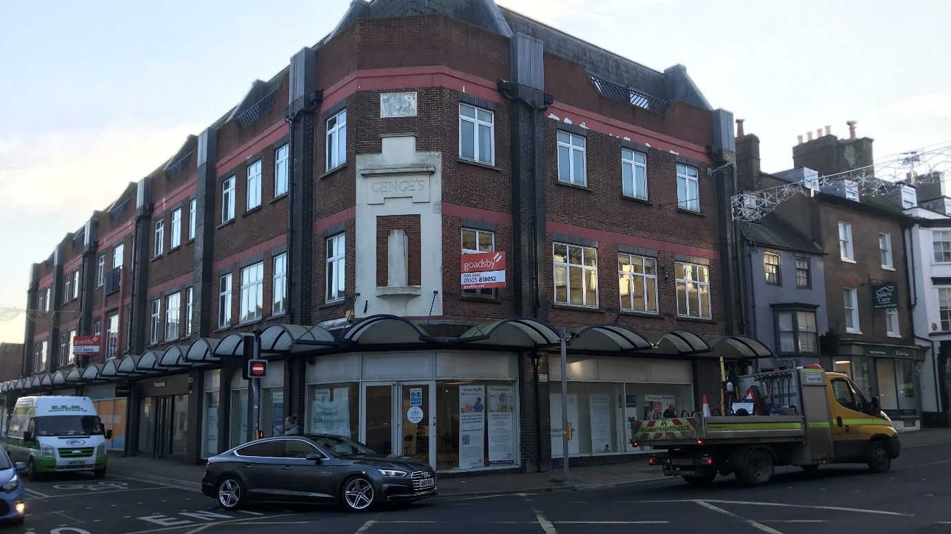 A car is parked in front of a large brick building.